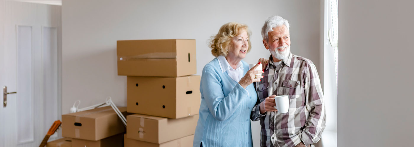 Senior couple drinking office while looking out their new window as they unpack from moving.