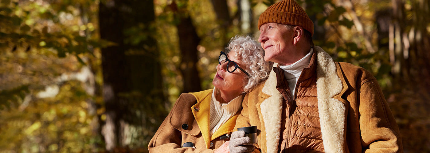 Senior couple sitting arm in arm drinking coffee while gazing into the beautiful fall foliage.