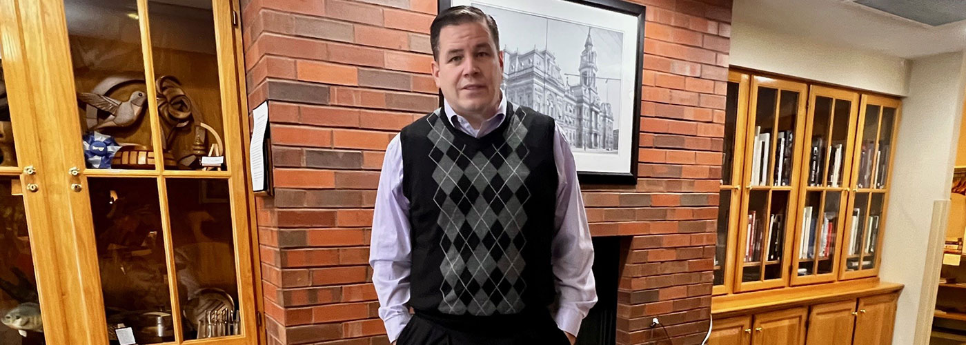 Jay Dorsey standing with his hands in his pockets looking at the camera while posed in front of a fireplace.