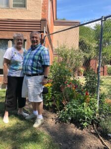 A senior couple standing outside by a fence and a wild flower garden.