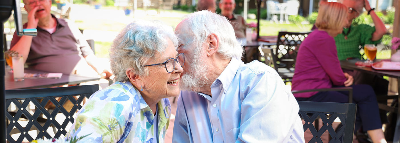 Senior couple talking lovingly while at an outside dining table.