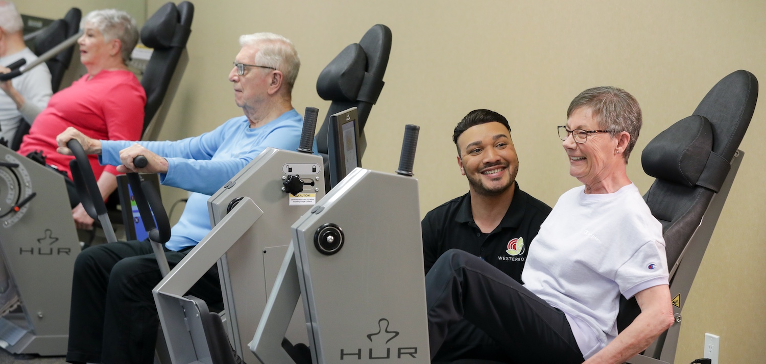 Senior woman on exercise equipment while an instructor helps.