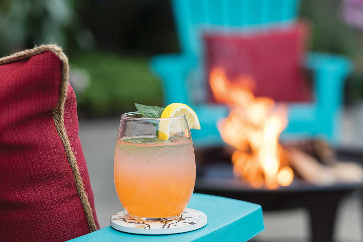 Mint julep sitting on the arm of an outdoor chair while a fire pit burns in the background.