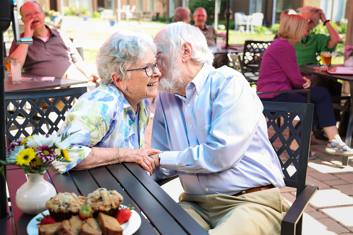 Senior couple whispering to each other while enjoying lunch at Westerwood's outdoor dining area.