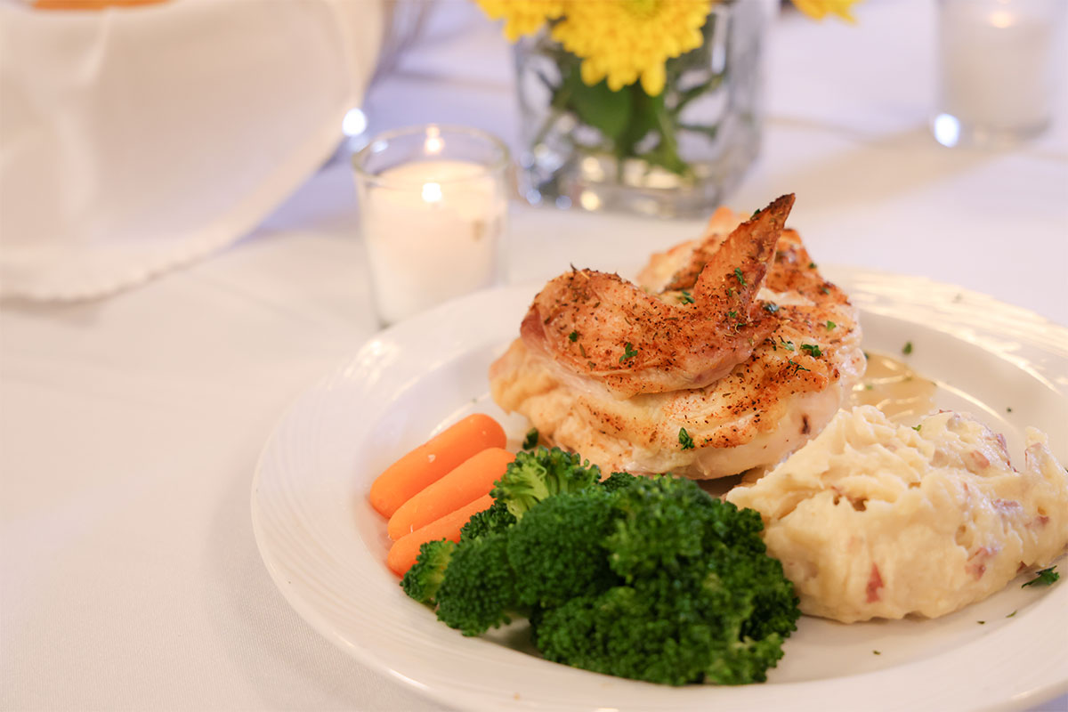Roasted chicken over mashed potatoes, carrots and broccoli.