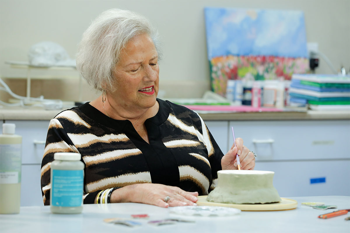 Senior woman painting a clay bowl.