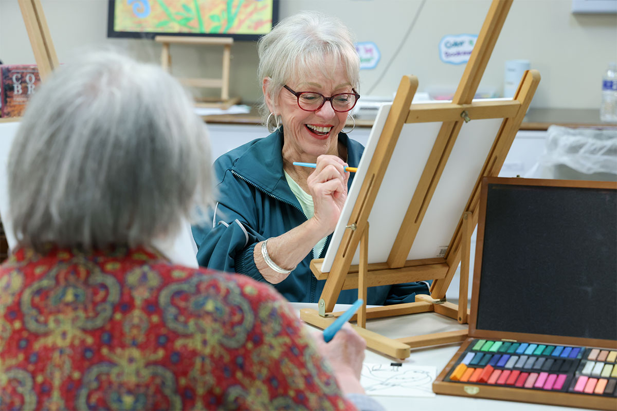 Women smiling and laughing while she paints a canvas.