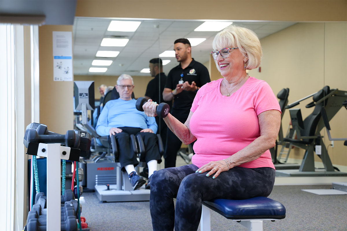 Woman seated on workout bench while lifting weights.