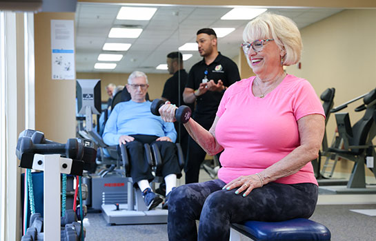 Senior woman lifting weights in fitness studio.