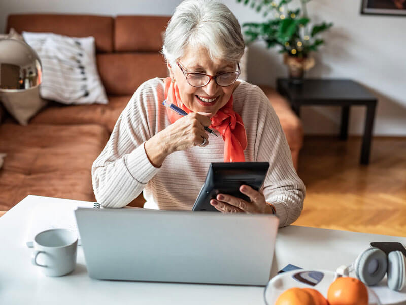 senior woman using a calculator while reviewing her finances on a laptop
