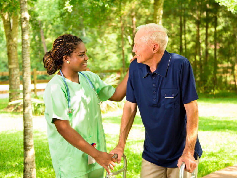 nurse assisting an older man with a walker