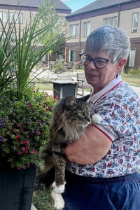 An older woman stands outside and holding a cat