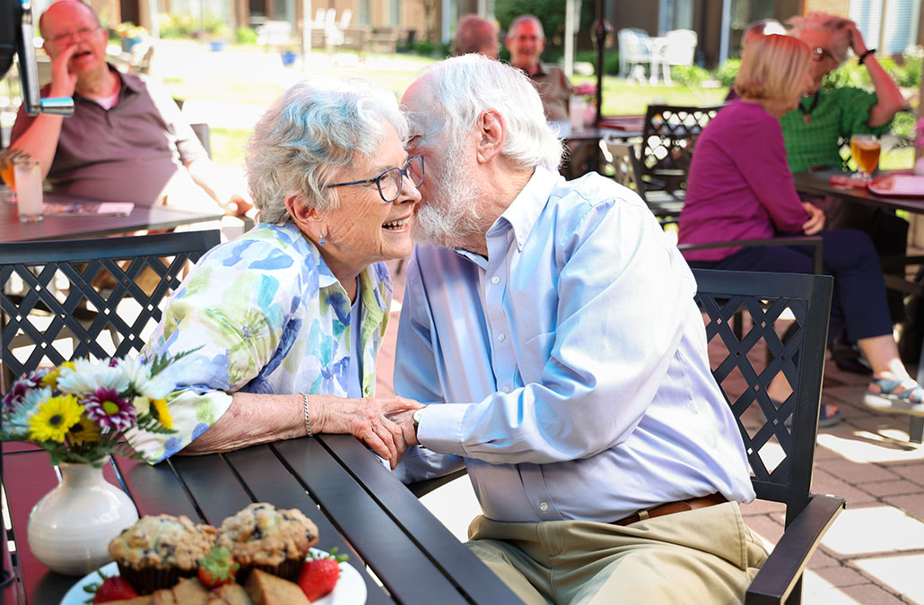 Couple-Whispering-1030x675-1 couple whispering while sitting at the Outdoor Community Patio