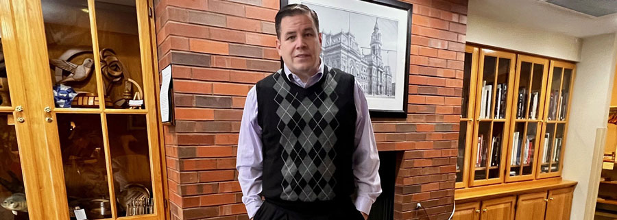A man poses in front of a fireplace