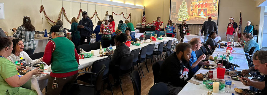 A large group of people seated at tables adorned with festive Christmas decorations, enjoying a holiday gathering.