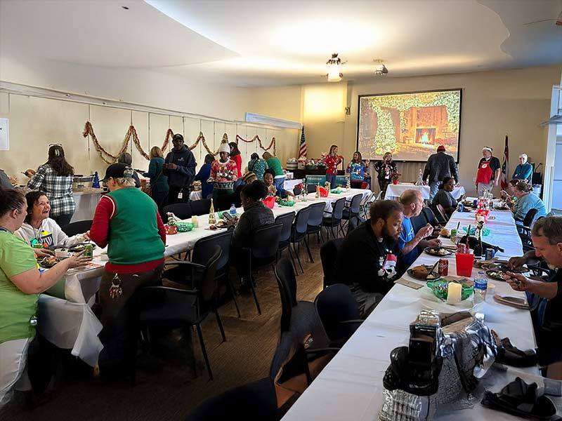 A large group of people seated at tables adorned with festive Christmas decorations, enjoying a holiday gathering.