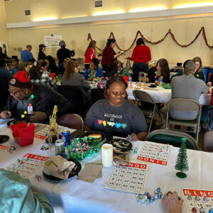 A large group of people seated at tables adorned with festive Christmas decorations, enjoying a holiday gathering.