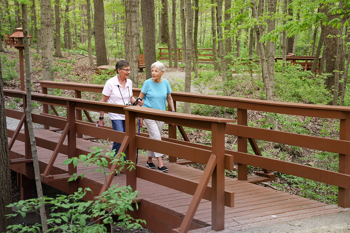 WW04292024-1104-1200x800-1 two women walking across a bridge in the woods