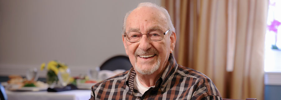 An older man with glasses smiles warmly at the camera