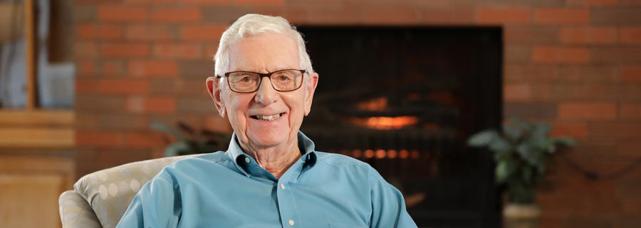 An older man with glasses smiles warmly at the camera