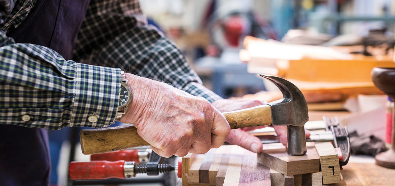 close up of senior man's hands holding hammer while woodworking